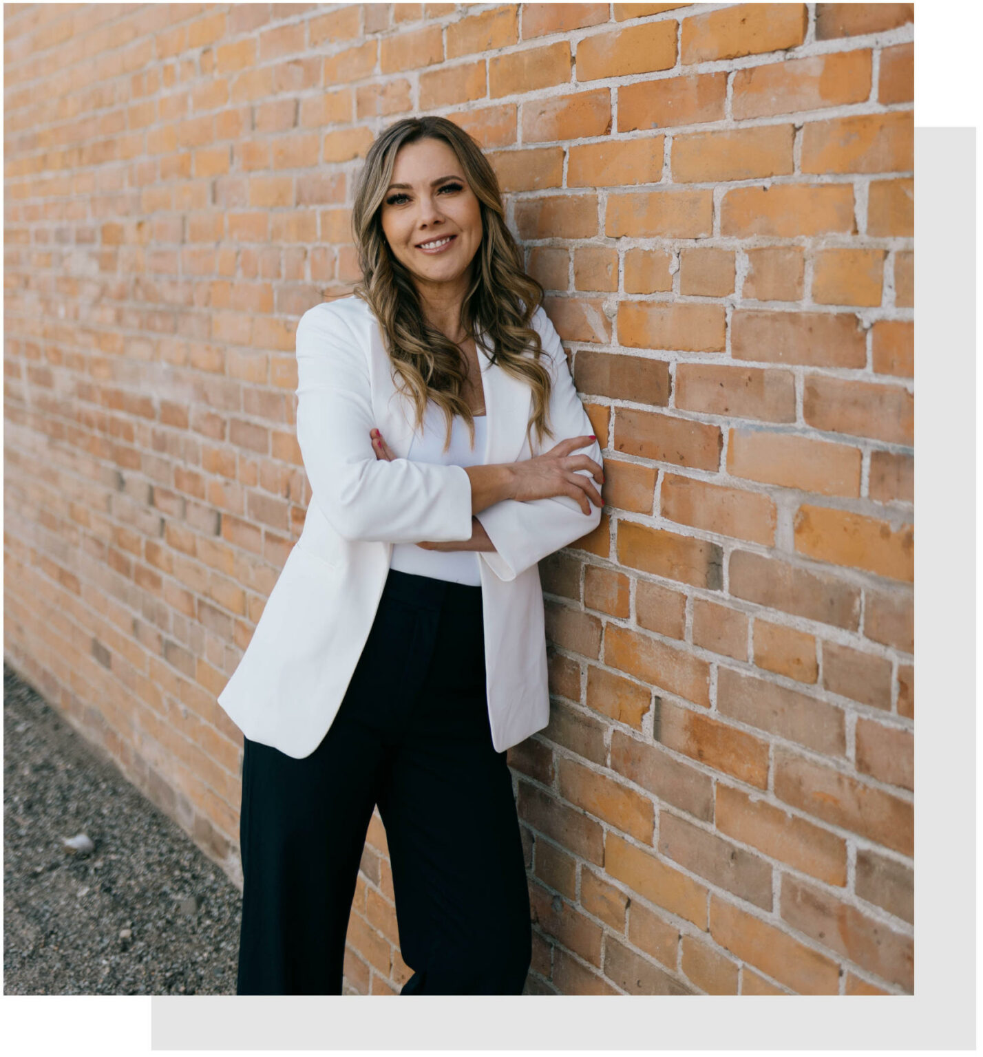 Kamloops mortgage consultant Sarah Park leaning against a brick call in a white coat and black pants.